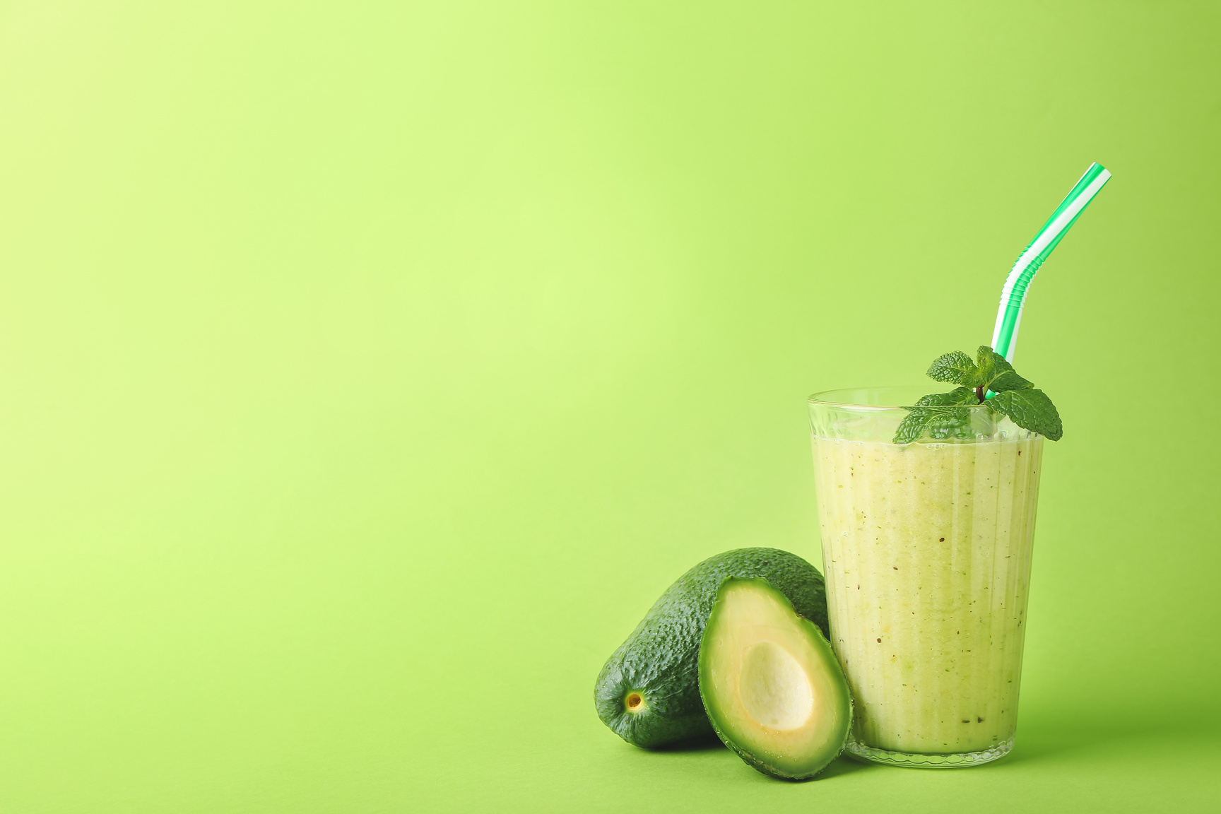 Glass of Healthy Green Smoothie and Avocado on Color Background